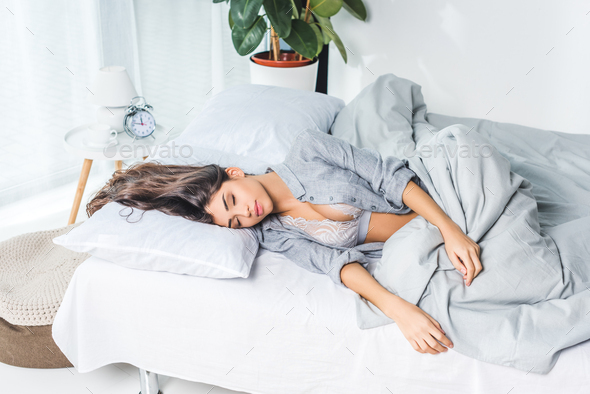 beautiful young woman in lingerie sleeping on bed Stock Photo by