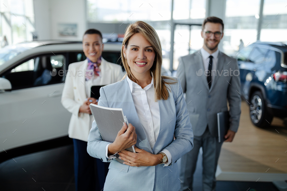 salesteam in dealership, three beautiful consultants or managers in elegant suit looking on camera.