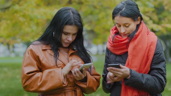 Two Young Women Holding Telephones in Hands Closeup Looking at Gadgets One Helps Other Download Cool alt