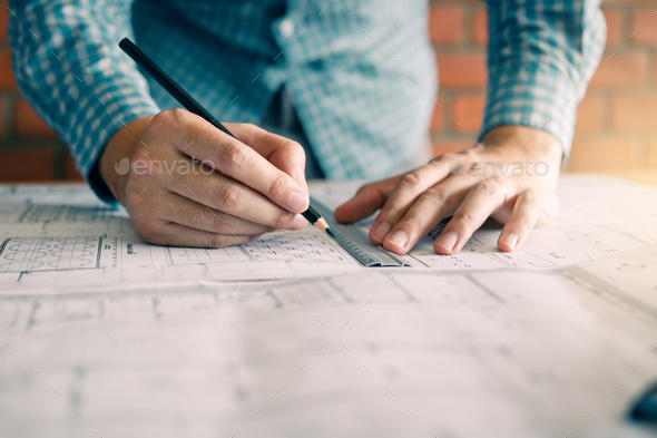 Engineering or architect reviewing blueprints and holding pencil on desk at home  office. Stock Photo by wutzkoh