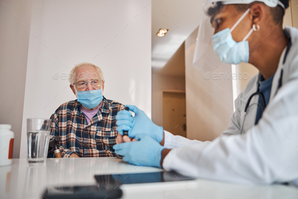 Geriatric physician taking a capillary blood sample from the patient - Stock Photo - Images