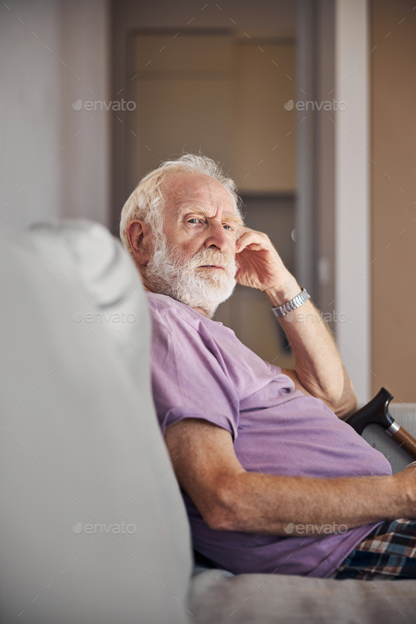 Thoughtful sad bearded male pensioner on the couch