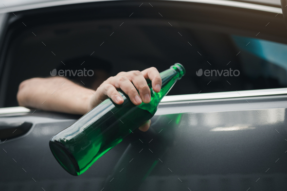 Asian man holding a bottle of beer outside the car while driving.