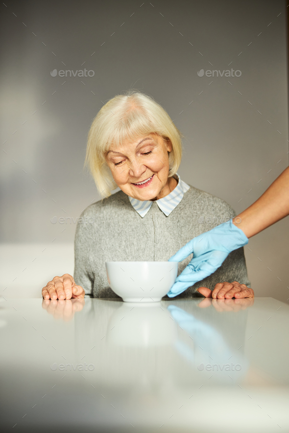 Joyful pensioner having her breakfast served by a volunteer