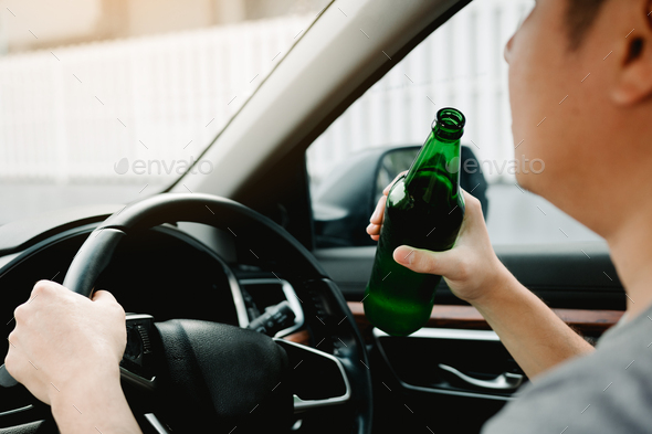 Asian men are breaking the traffic rules by holding a bottle of beer and drinking while driving.