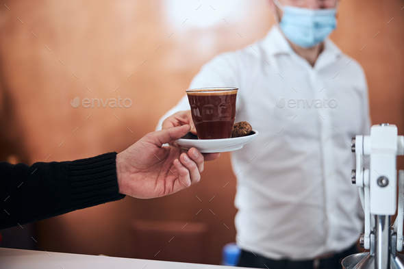 Waiter serving coffee to man during quarantine