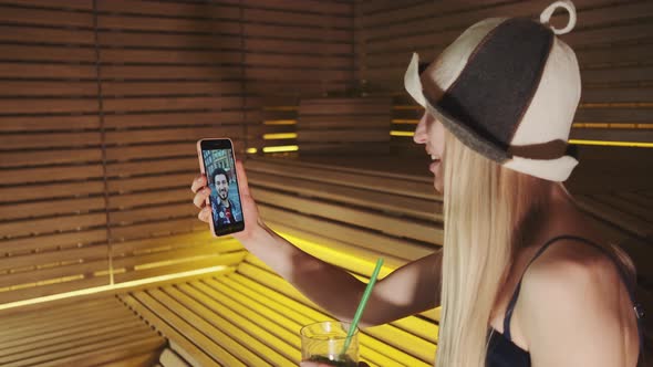 Profile View of Blonde Woman in Sauna Making Video Call with Man From Other Place alt
