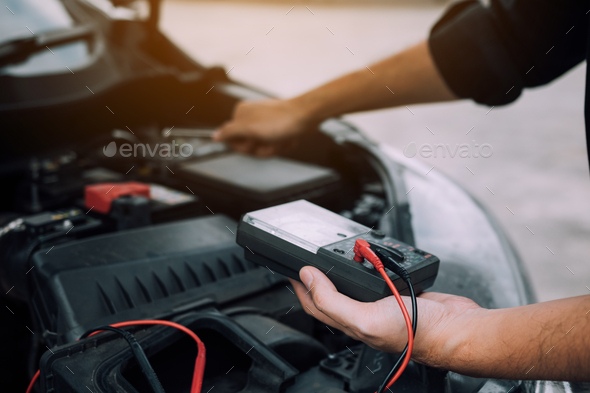 The car mechanic is carrying a battery meter and checking the general condition of the engine.