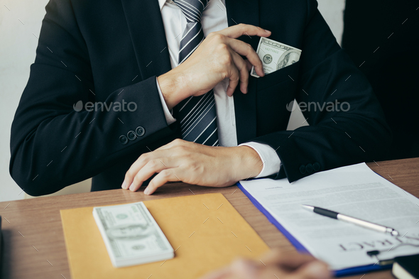 Businessman putting stack of money bills in his suit coat pocket.