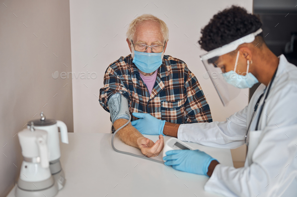 Focused geriatric physician staring at the automatic manometer - Stock Photo - Images
