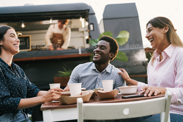Multiracial friends eating at food truck table outdoor