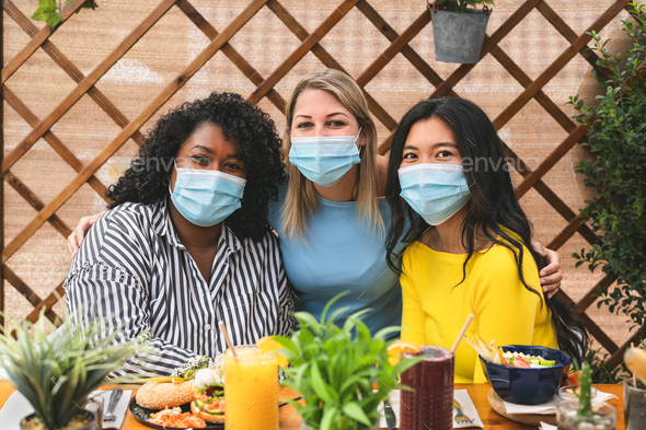 Multiracial friends wearing face mask while having healthy lunch in coffee brunch bar