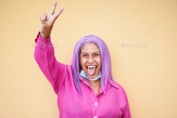 Cool old woman with purple hairs doing peace symbol with hand and tongue
