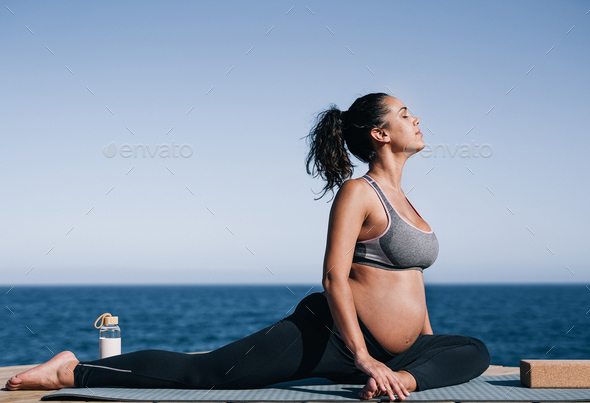 Pregnant woman doing yoga exercise routine next to the beach Stock
