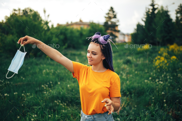 Young beautiful girl unusual bright appearance throwing out a medical mask in a yellow shirt in the