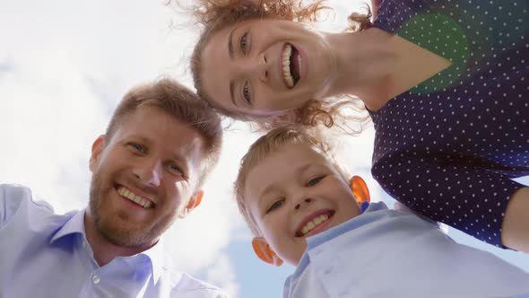 Bottom View of Happy Mother Father and Son Look Down at Camera Outdoors alt