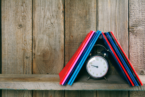 Alarm clock and writing-books on a wooden shelf. - Stock Photo - Images