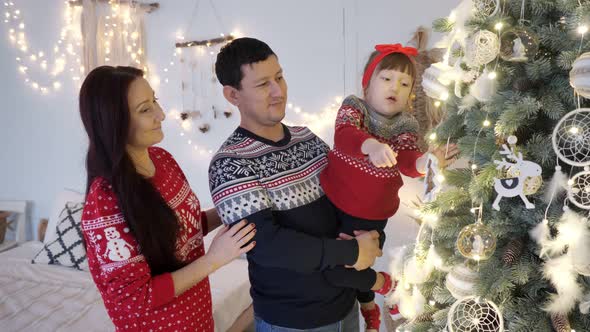Parents with Daughter Decorate Illuminated Christmas Tree alt