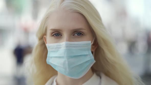 Portrait of a Beautiful Blonde Haired Young Woman Wearing Protective Medical Face Mask and Standing