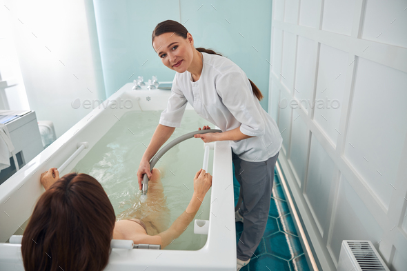 Smiling woman caring about the female in whirlpool spa bath