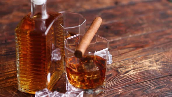 Bottle of Whiskey with Two Glasses and Cuban Cigar Placed on Rustic Wooden Table alt
