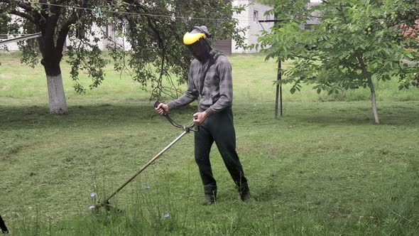Worker with a gas mower in his hands, mowing grass in front of the house. alt