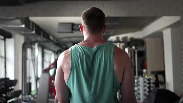 A man in a gym standing with his back raises a barbell in front of him alt