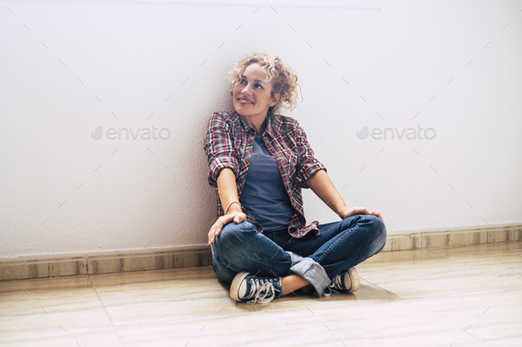 Happy single adult woman sit down on the floor of empty new house property - female lady