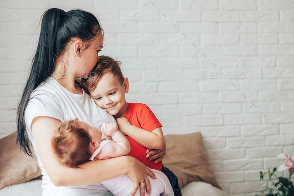 Young mother with two children and one kiss on the forehead Stock Photo ...