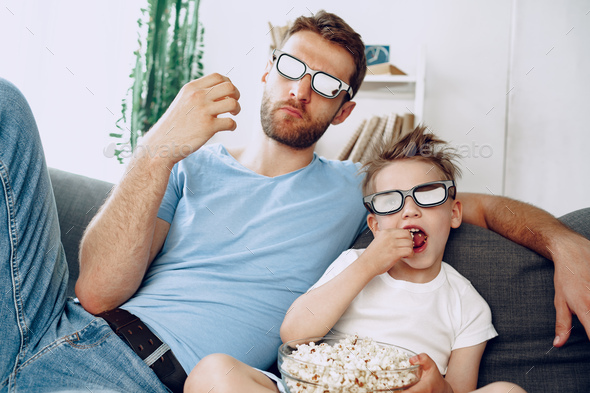 Father and son watching movies at home in 3d glasses and eating popcorn