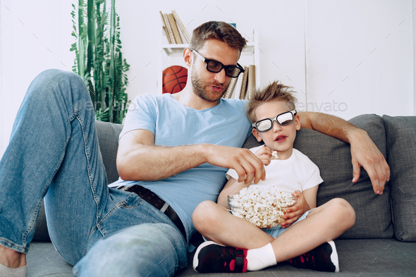 Father and son watching movies at home in 3d glasses and eating popcorn