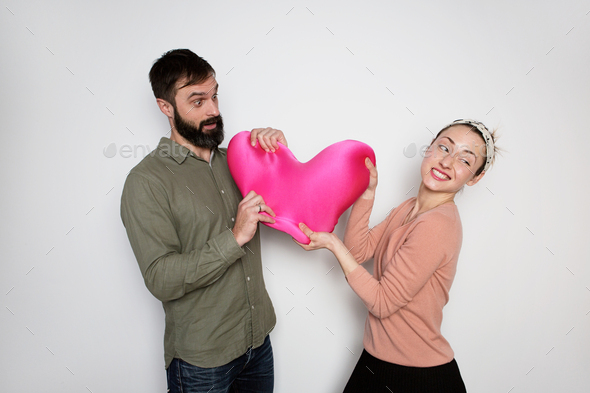 Bearded man and young girl play with red soft toy heart. Couple in love tears big heart