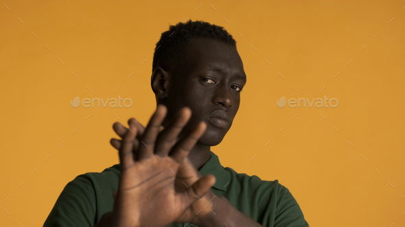 African American man looking serious showing stop gesture over yellow background. Don\'t want