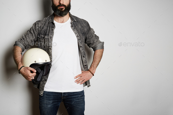 Handsome Brutal bearded male model poses in black jeans shirt and t-shirt  with moto helmet in hands Stock Photo by Eyecan2