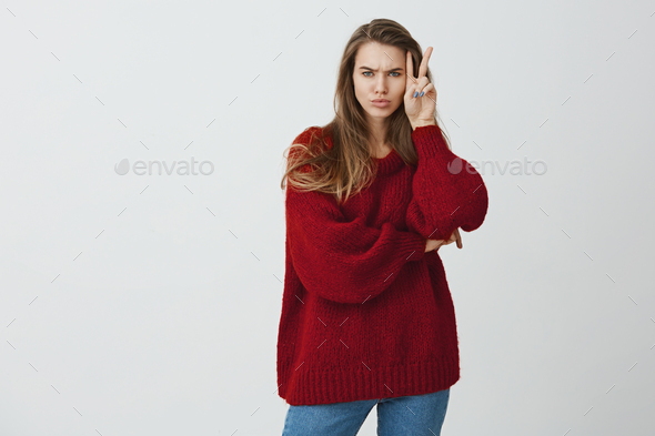Not a doll to smile all time. Studio shot of stylish good-looking woman in loose sweater showing v