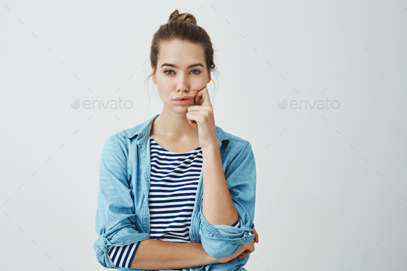 Girl need to find answer. Charming young caucasian woman with bun hairstyle holding fingers on cheek