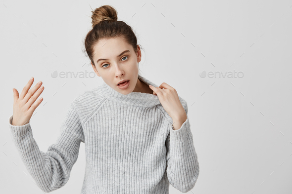 Adult girl 20s having heat stroke gesturing she needs fresh air. Woman with hair in bun wearing warm
