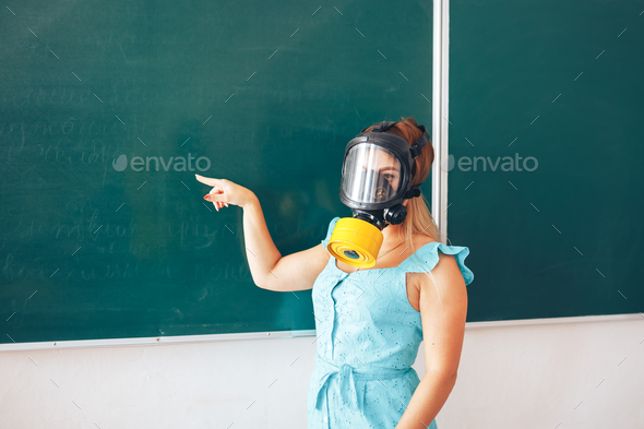 Young teacher in a medical mask holding a pointer in her hand and points to a white board, back to