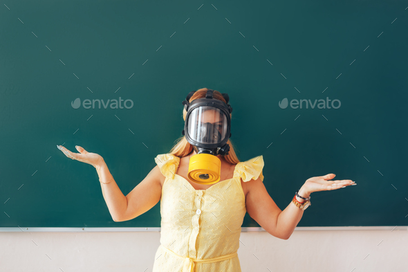 Young teacher in a medical mask holding a pointer in her hand and points to a white board, back to