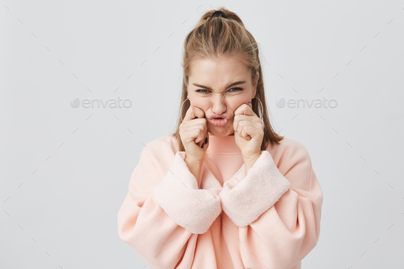 Charming, frowning her face, stylish European girl with blonde hair dressed in pink sweatshirt