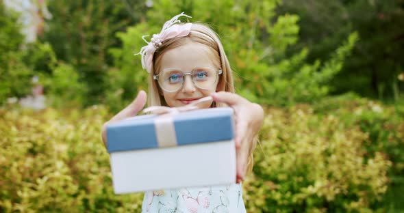 A Beautiful 7Yearold Girl with Glasses Give a Gift in a Blue Box with a Bow alt