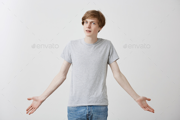 Stylish fair-haired caucasian guy in casual clothes, with blue eyes, shrugging shoulders with