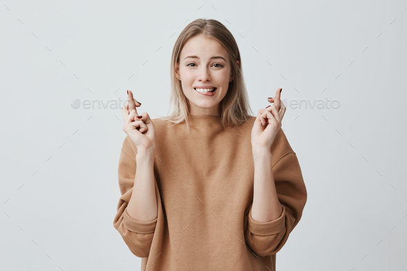 Portrait of wishful young woman in casual clothes with blonde dyed hair, crossing her fingers