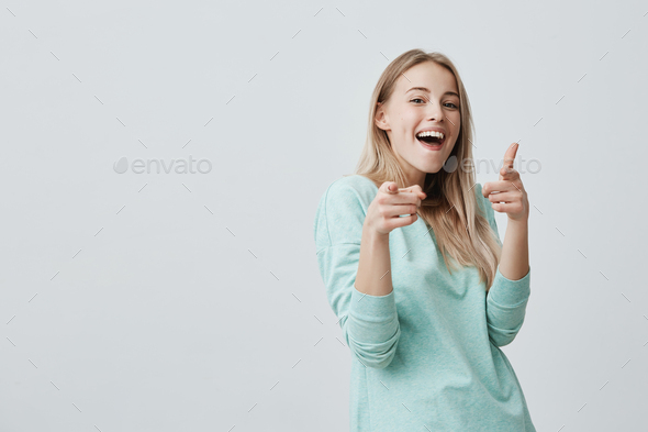 Happy positive joyful blonde woman with dyed hair smiling pleasantly pointing with index finger at