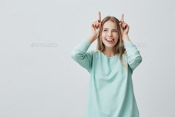Positive funny European woman with blonde dyed hair dressed in blue sweater smiling broadly holding
