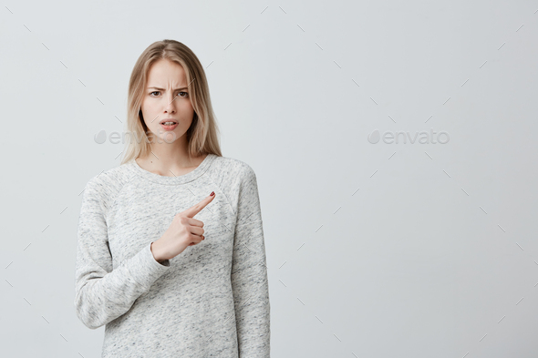Beautiful woman with blonde dyed hair looking at something with disgust and dissatisfaction pointing