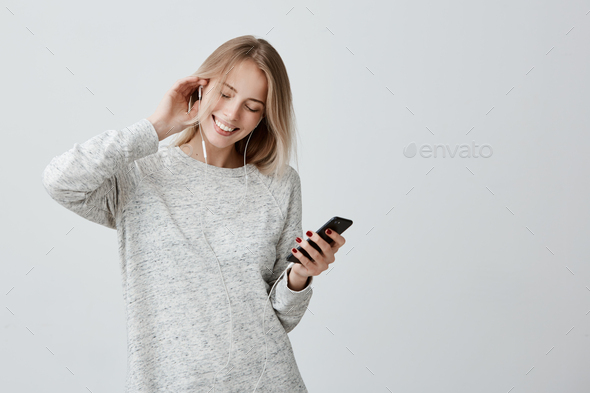 Music, happiness and technology concept. Lovely teenage girl has blonde dyed hair, listens to music