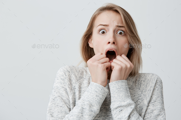 Astonished terrified attractive young blonde with dyed hair female in sweater having scared face