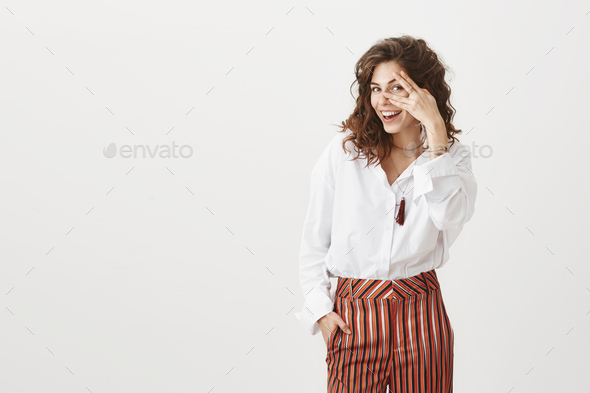 I see everything. Beautiful european woman with curly hair in stylish blouse and striped trousers
