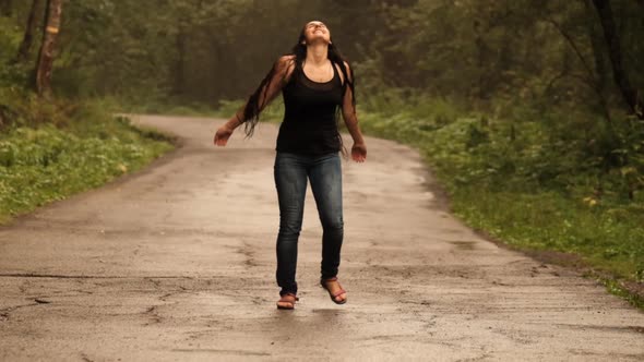 Slow Motion of a Young Caucasian Woman Enjoying the Summer Rain Raising Her Hands on a Road in the